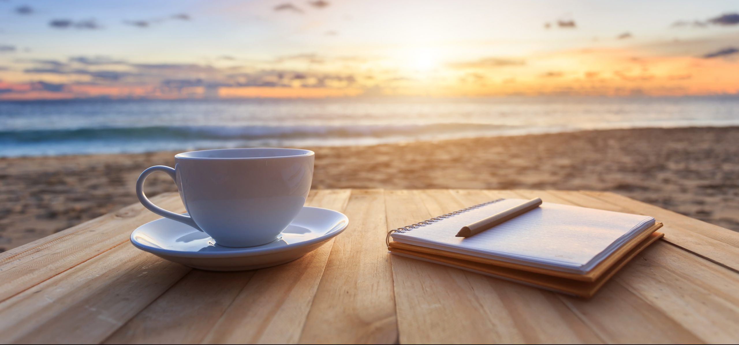 Coffee and note pad on table overlooking beach sunset